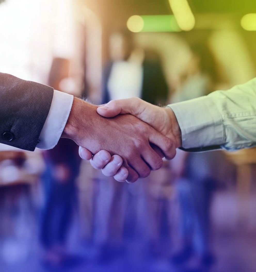 A close-up of a firm handshake between two businessmen in a modern office setting, representing a partnership or agreement, with a blue and light green color overlay.